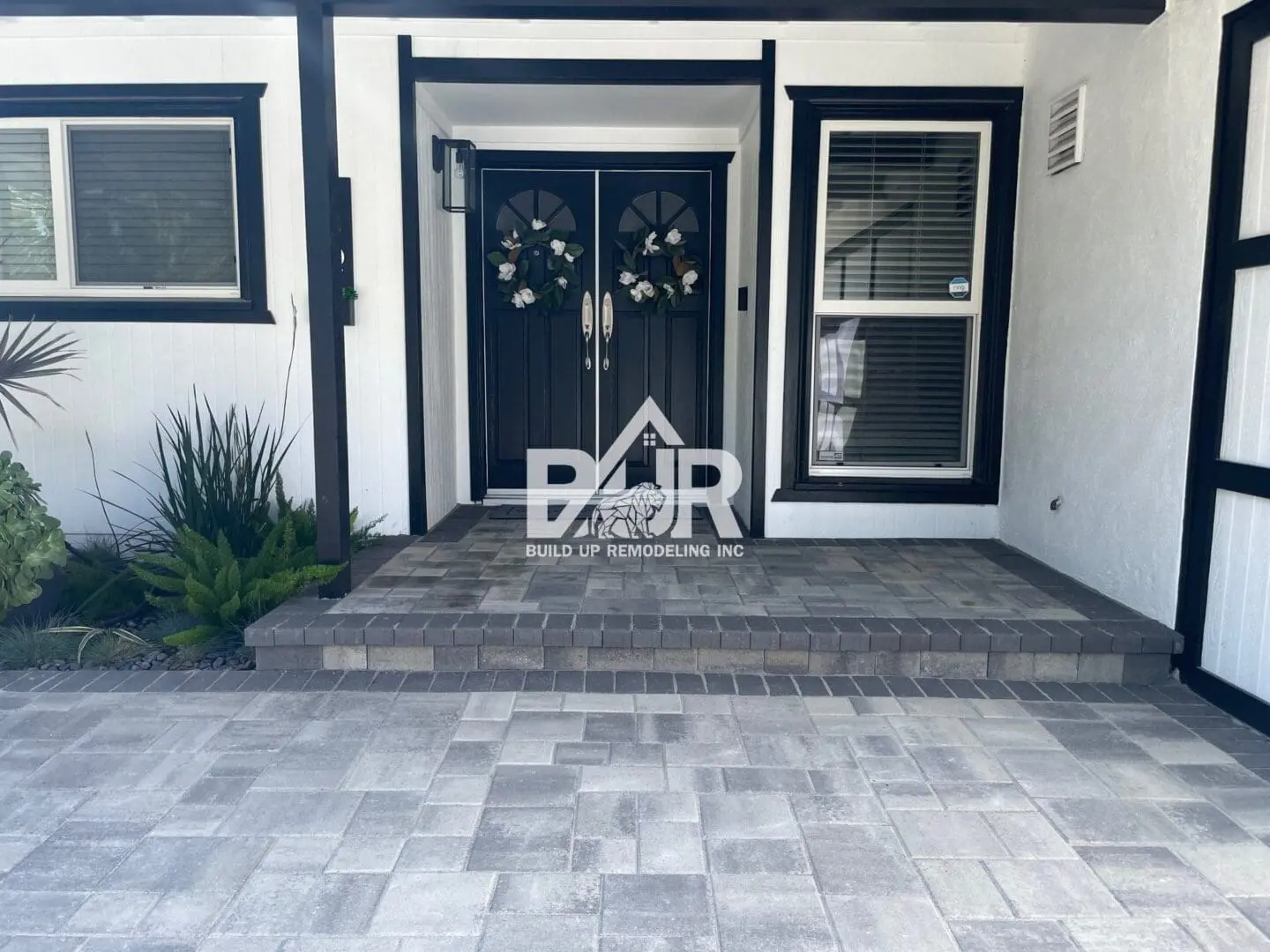 Front porch with black double doors and decorative wreaths at a modern home.
