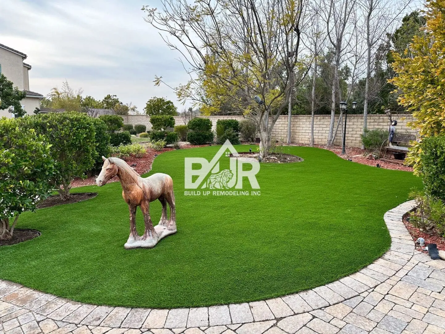 A small horse statue stands on a green lawn near a stone pathway.
