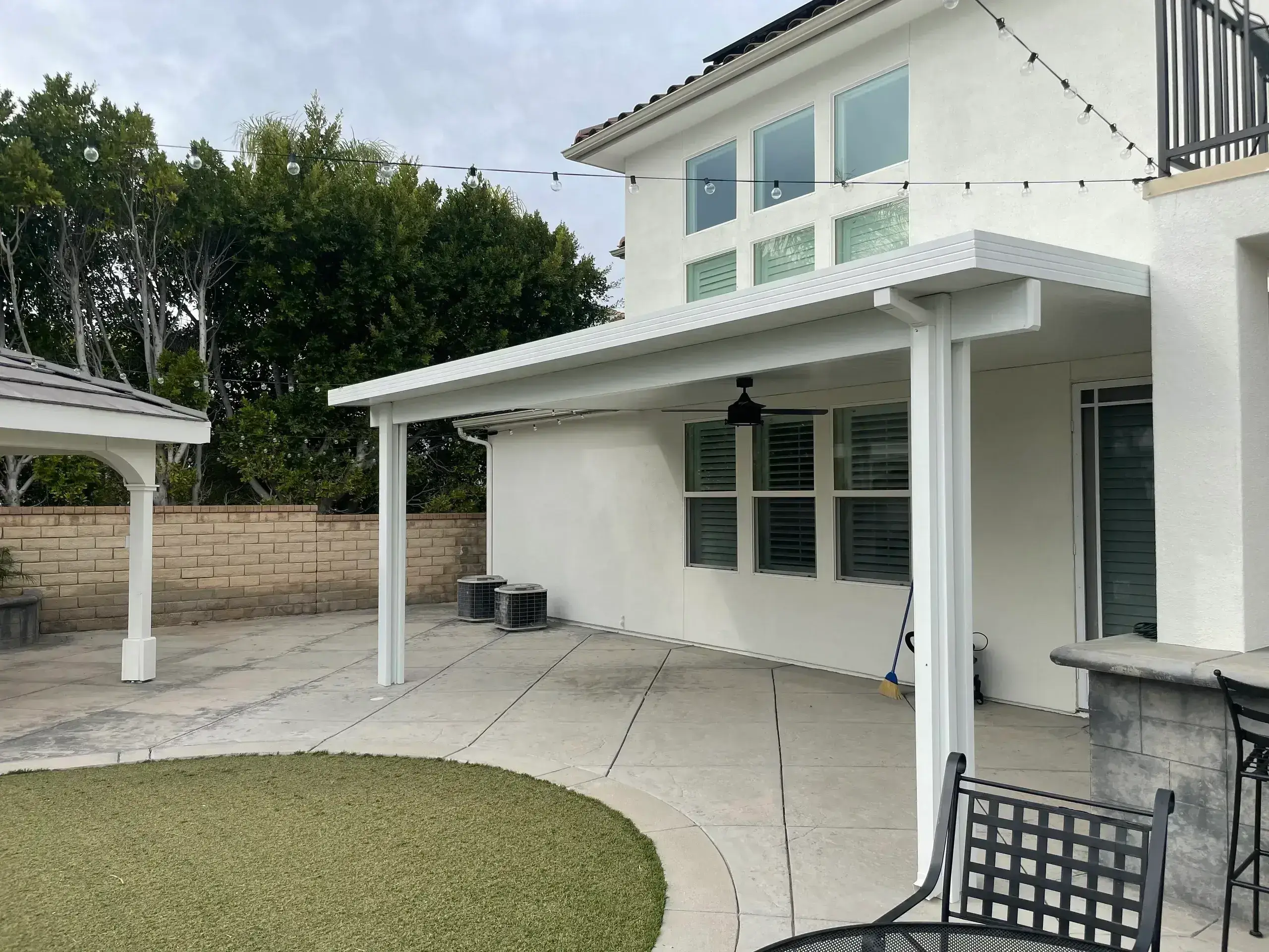Backyard patio with white pergola and lawn.
