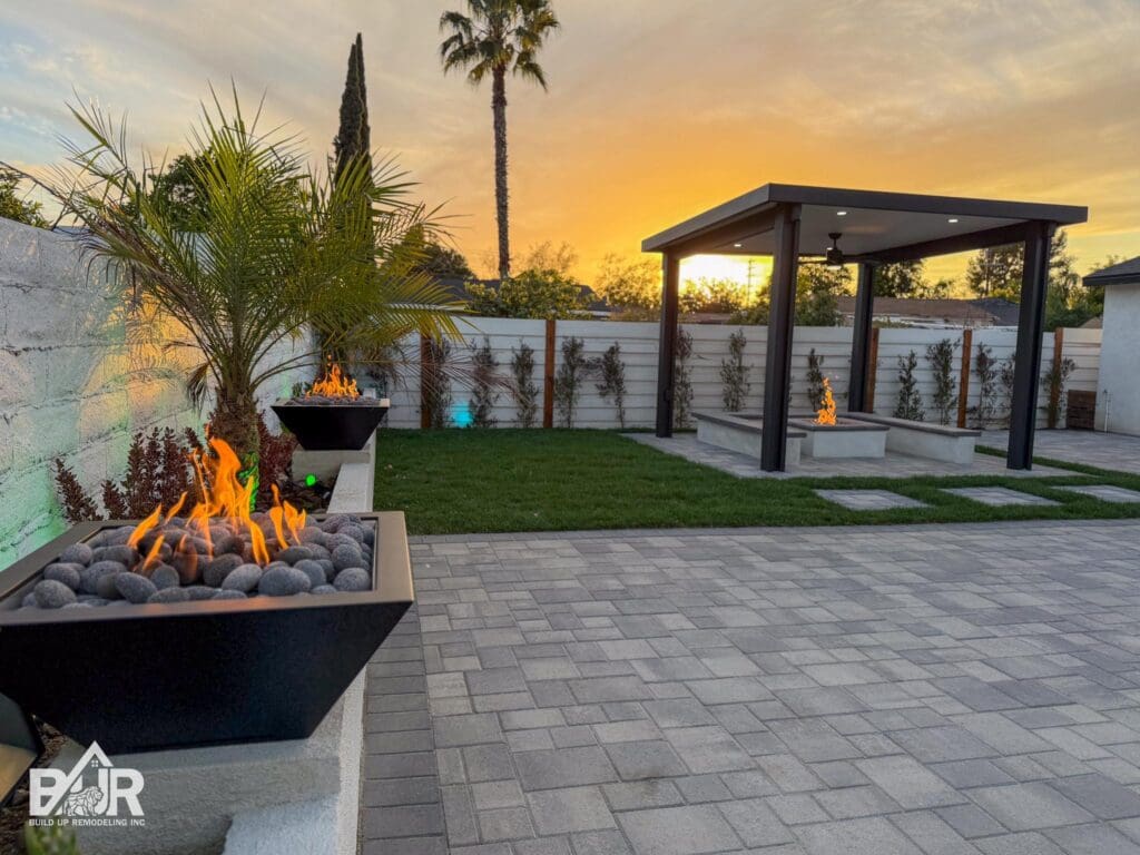 BACKYARD WITH PATIO COVER, FIRE PIT, GRAY CHARCOAL PAVERS AND FIRE BALLS ON TOP OF PLANTER WALL WRAPED BY SOD