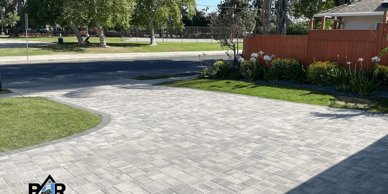 A paved driveway leading to a street bordered by grass and trees.