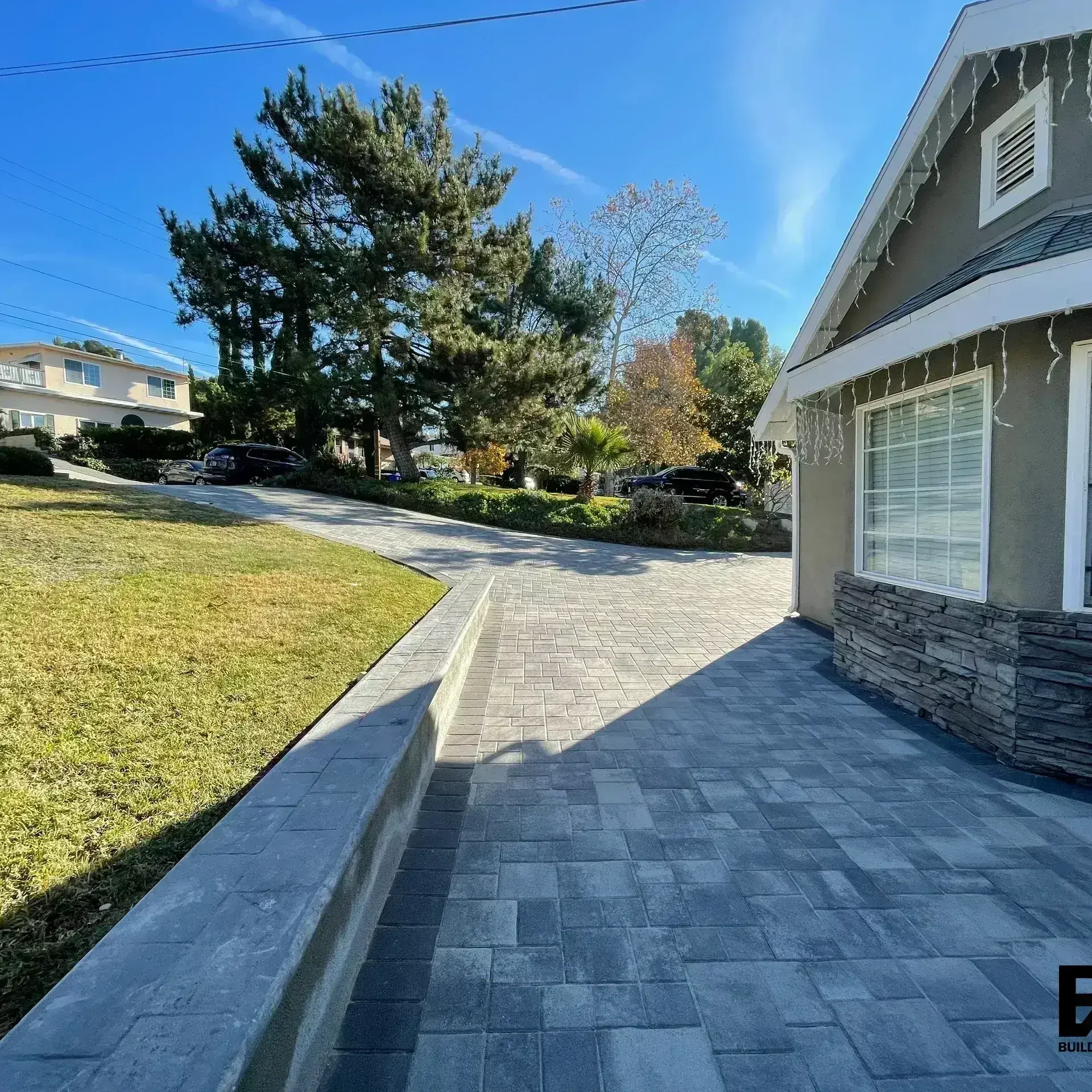 A paved driveway leading to a house with a stone exterior and a landscaped yard.